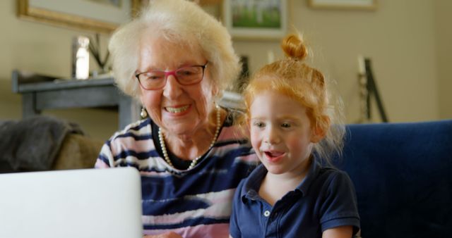 Close up of a grandmother and granddaughter using digital tablet in living room at home. Happy smiling grandmother and granddaughter watch a show on a computer while sitting on the sofa.
