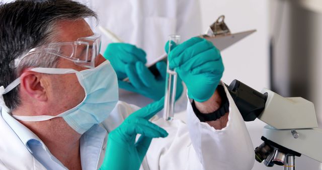 Scientists working in a laboratory, analyzing samples using a microscope and a test tube. The individuals are wearing safety goggles, surgical masks, and gloves while performing their experiments. Ideal for illustrating medical research, scientific studies, or laboratory procedures.