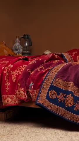 Vertical video panning across low bed with ornate red blanket and intricate border