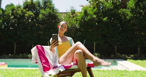 Woman relaxing by pool using smartphone on sunny day