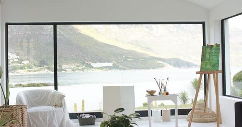 Sunlit coastal art studio with full-height windows framing bay and minimalist interior