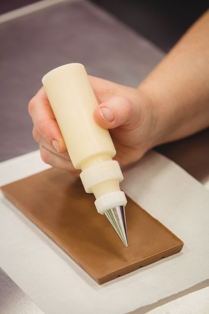 Worker writing with piping bag on chocolate plaque in kitchen