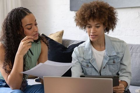 African american friends collaborating on laptop and paperwork in cozy living room