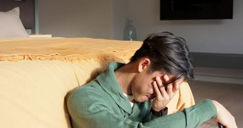 Man Seated by Bed Contemplating in Cozy Minimalist Bedroom Interior