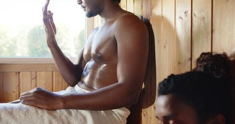 Sunlit sauna couple relaxing on wooden bench, sweating and enjoying rustic spa wellness