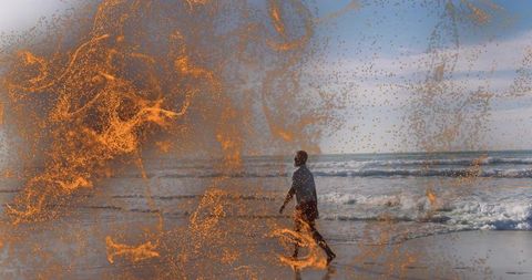 Man walking along ocean shoreline overlapped with abstract orange sparks