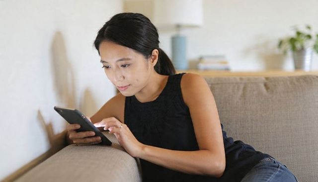 Young woman relaxing on sofa using smartphone for messaging, browsing in cozy living room