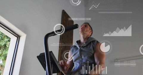 Mid-adult man gasping on upright bike while tracking performance with digital fitness data
