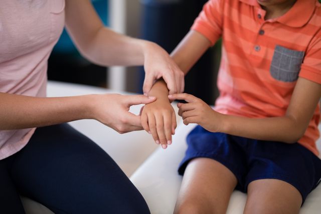 Therapist examining boy's hand in hospital. Useful for healthcare, pediatric care, medical treatment, and professional consultation themes.