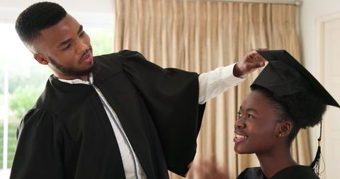 Excited couple celebrates graduation at home in caps and gowns