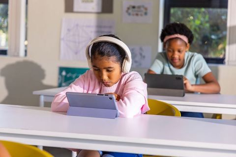 Focused multiracial schoolchildren using tablets and headphones in classroom learning