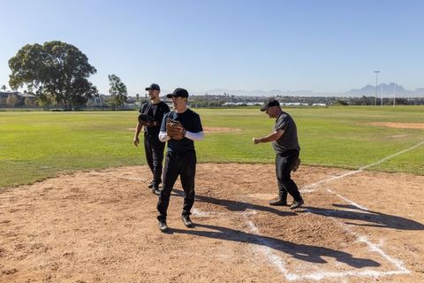 Three Baseball Players Warming Up at Home Plate on Sunny Infield During Team Practice