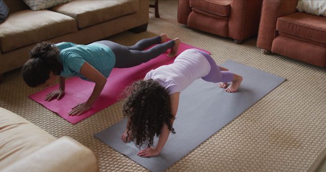Biracial mother and daughter practicing yoga in living room. domestic life and family leisure time concept.