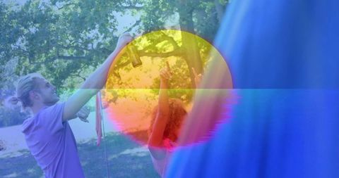 Friends attaching rope and raising blue fabric canopy in park with vibrant circular light overlay