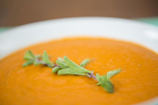 This image showcases a close-up view of a creamy pumpkin soup garnished with fresh herbs. Ideal for use in culinary blogs, recipe websites, health and wellness articles, or autumn-themed promotions. Perfect for illustrating homemade and nutritious meal options.