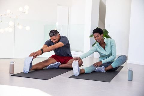 Diverse workout partners stretching hamstrings in modern living room