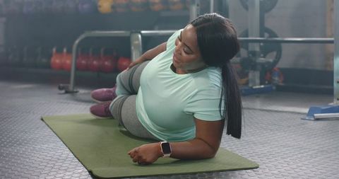 Mid-adult african american woman practicing side plank on mat in gym for core strength and balance