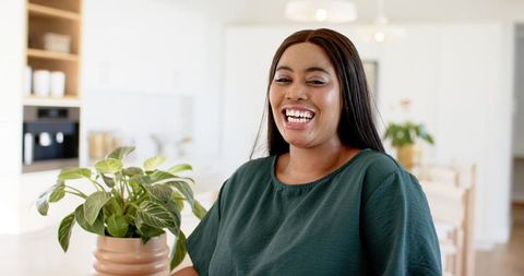 African american woman smiling in bright kitchen near potted plant, lifestyle portrait