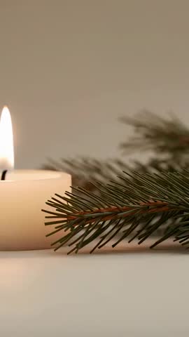 Flickering Votive Candle Casting Warm Glow Beside Pine Branch Vertical Video