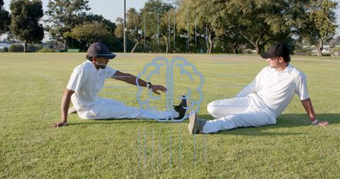 Two cricketers stretching on sunlit outfield wearing white kits and caps during warm-up