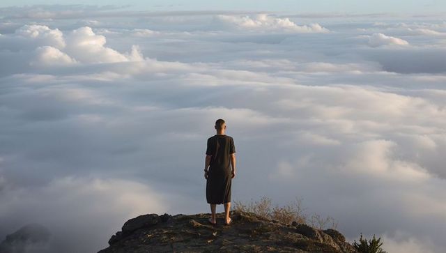 Solitary hiker standing on cliff edge over expansive sea of clouds at sunrise