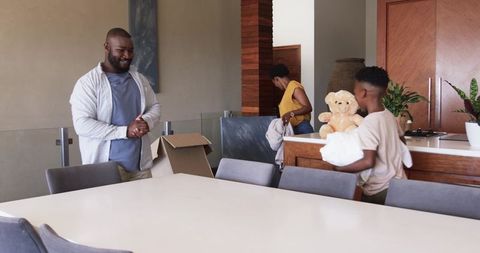 African American family unpacking in modern kitchen carrying teddy bear and moving boxes