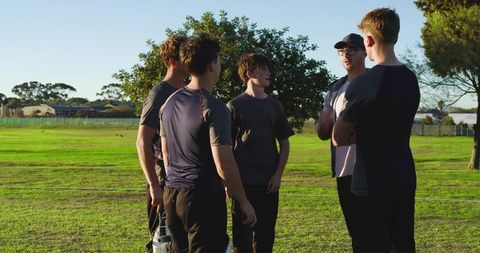 Coach rallying teen baseball team in pregame huddle, motivating players on field