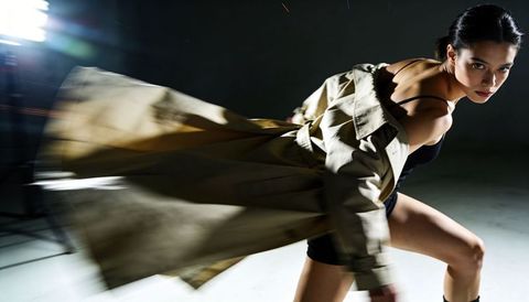 Lunging female model wearing flowing trench coat revealing bodysuit in dramatic motion