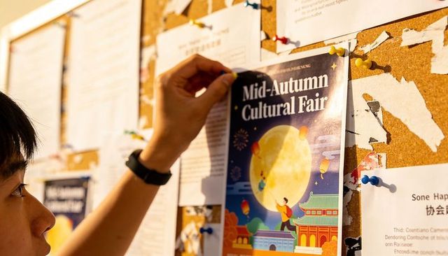 Asian student pinning mid-autumn cultural fair poster on university noticeboard