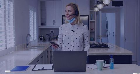 Woman Utilizing Home Workspace Holding Phone and Laptop