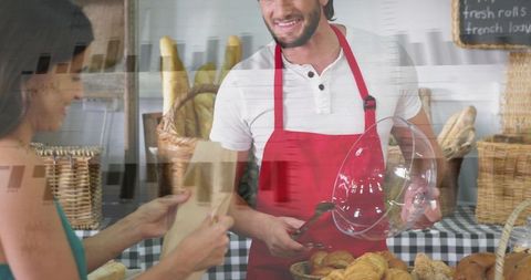 Smiling bakery vendor serving croissants with red apron at busy farmers market stall