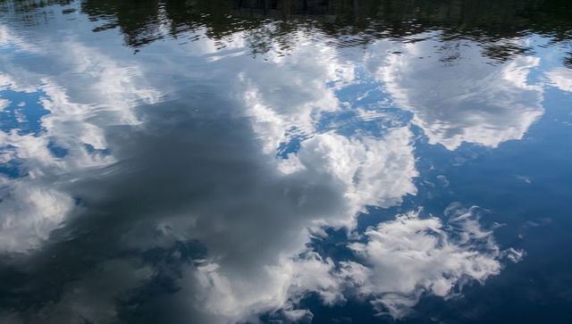 Cumulus cloud reflection rippling on calm lake surface for tranquil sky background