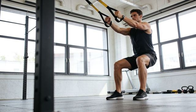 Athletic man performing trx suspension squat pull workout in sunlit minimalist gym space