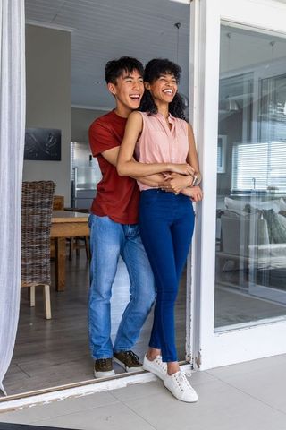 Smiling multiracial couple hugging and entering home through sliding glass door