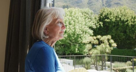 Senior woman standing at glass door gazing outdoors