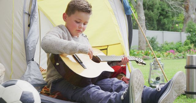 Caucasian boy sitting in tent in garden and playing guitar - Download Free Stock Photos Pikwizard.com
