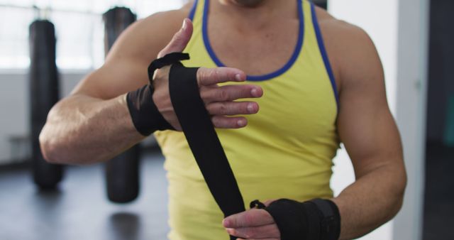 Mid section of caucasian male boxer wrapping boxing tape on his hands at the gym. sports, training and fitness concept