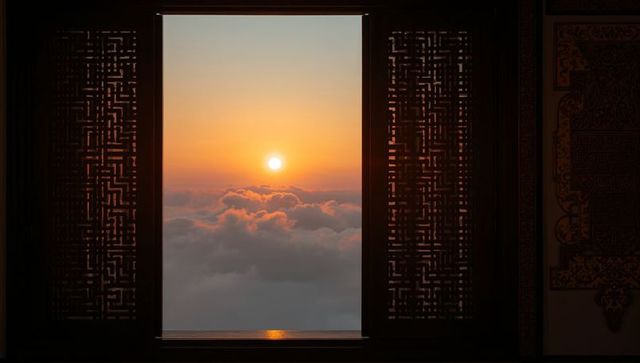 Sunrise above clouds framing ornate wooden lattice window, historic temple interior at dawn