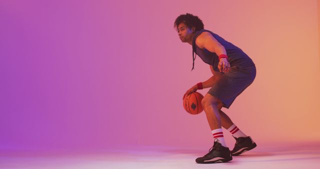 Image of biracial male basketball player with ball on orange to pink background. Sports and competition concept.