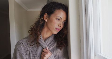 Thoughtful woman looking out window in cozy sweater