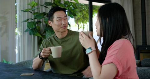 Asian couple enjoying morning coffee and conversation in bright modern living room
