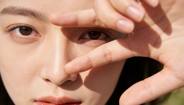 Sunlit closeup asian woman shielding eyes with hand casting finger shadows natural skincare