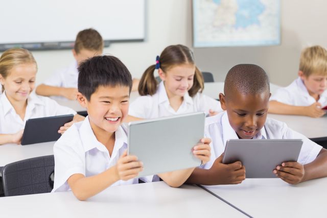 Children in an elementary school classroom are using digital tablets for learning activities. The students are engaged and smiling, indicating a positive and interactive learning environment. This image can be used for educational websites, technology in education promotions, school brochures, and articles about modern teaching methods.