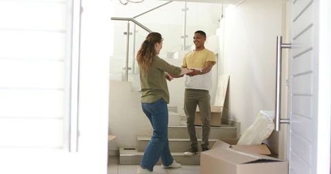 Young interracial couple exchanging keys while moving into modern home with boxes on stairs