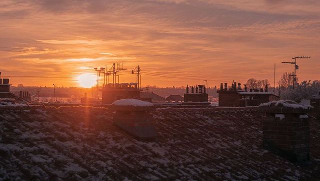 Snow-dusted rooftop glowing at sunset with chimneys and antennas