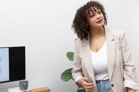 Curly-haired professional presenting sketch on monitor at modern office desk