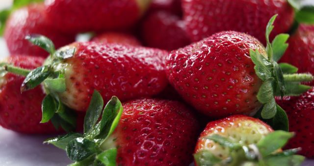 This colorful close-up image captures fresh, ripe strawberries with green stems, emphasizing their juicy, textured surface. Ideal for use in food and beverage marketing materials, health and nutrition articles, recipe blogs, or advertisements for organic produce.