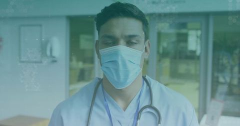 Standing hispanic clinician wearing surgical mask and stethoscope at clinic reception