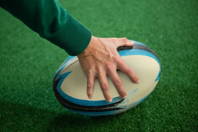 Cropped hand holding rugby ball on playing field