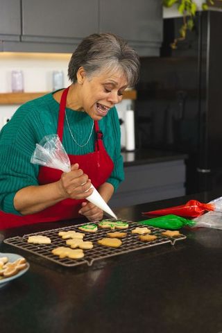 Senior woman joyfully decorating cookies with icing in home kitchen